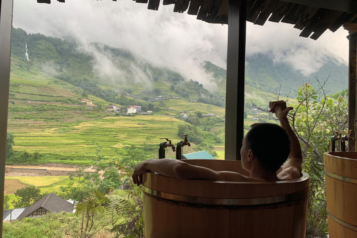 Tourist enjoying a Red Dao herbal bath experience in a rustic wooden tub in Ta Phin village